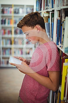 Happy schoolboy using digital tablet in library