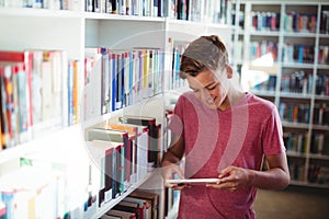 Happy schoolboy using digital tablet in library