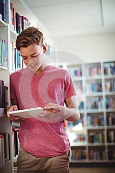 Happy schoolboy using digital tablet in library