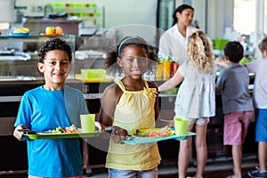 Happy schoolchildren holding food tray in canteen