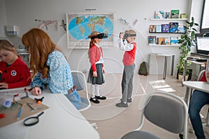 Happy schoolchildren wearing virtual reality goggles at school in computer science class