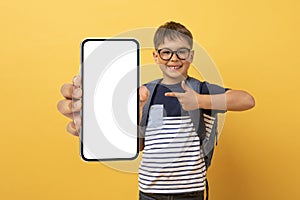 Happy schooler caucasian boy showing cell phone with blank screen