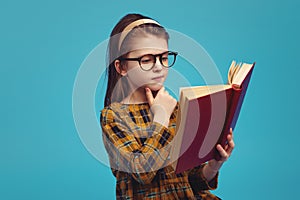 Happy schoolgirl in eyeglasses reading book and doing homework