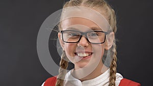Happy schoolgirl in eyeglasses smiling at camera against blackboard, education