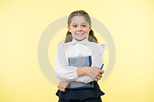 Happy schoolgirl hold book on yellow background. Little girl smile with textbook and pen. Confident in her knowledge