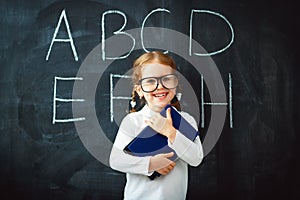 Happy schoolgirl preschool girl with book near school blackboard