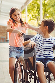 Happy schoolgirl pushing a boy on wheelchair