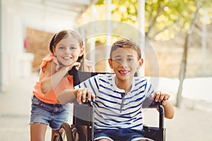 Happy schoolgirl standing with schoolboy on wheelchair