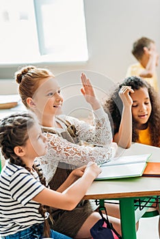 happy schoolgirls sitting at classroom during lesson