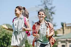 Happy schoolkids with backpacks smiling while running in park