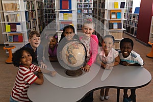 Happy schoolkids with globe looking at camera in school library