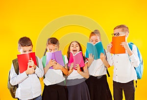 Happy schoolkids standing with colorful books isolated on yellow background. Kids hiding face behind books