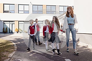 Happy schoolkids in uniforms with teacher walking at a schoolyard.
