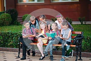 Happy Schoolmates Portrait. Schoolmates seating with books in a wooden bench in a city park and studying on sunny day.