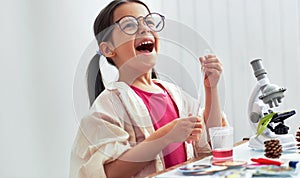 Happy scientific little girl wearing eyeglasses, working with microscope. The kid learning science in the school laboratory. Child