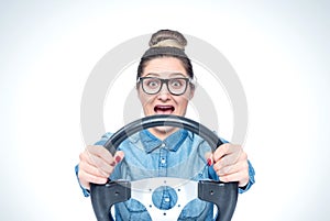 Happy screaming young girl with glasses and car steering wheel, front view, auto concept