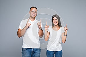 Happy screaming young lovely couple pointing and looking up with open mouths over gray background