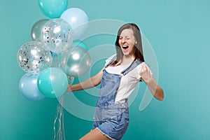 Happy screaming young woman with closed eyes doing winner gesture, celebrating and holding colorful air balloons