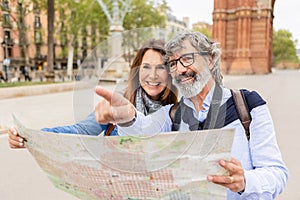 Happy senior adult couple holding city map while visiting Barcelona on vacation