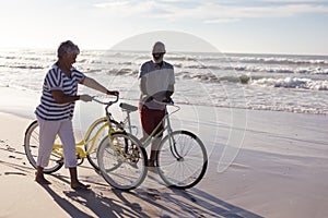 Happy senior african american couple with bicycles walking together on the beach