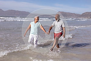 Happy senior african american couple holding hands and having fun on the beach