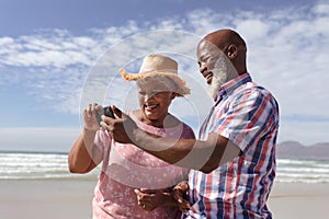 Happy senior african american couple using smartphone at the beach