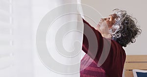 Happy senior african american woman widening curtains in bedroom