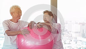 Happy senior Asian couple have fun with gym yoga ball class