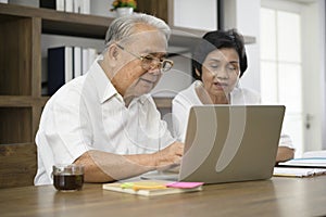 Happy senior Asian couple is spending time on surfing  the internet and talking with family on webcam,  retirement concept