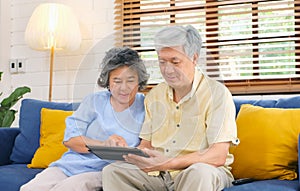 Happy senior asian couple using digital tablet computer sitting on sofa at home living room background, senior people and