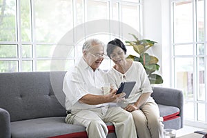 Happy senior Asian couple is using tablet and talking with family on webcam at home, retirement concept