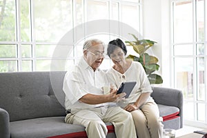 happy senior Asian couple is using tablet and talking with family on webcam at home, retirement concept