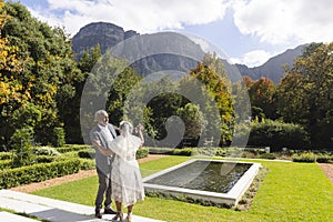 Happy senior biracial bride and groom dancing in garden at sunny wedding ceremony, copy space