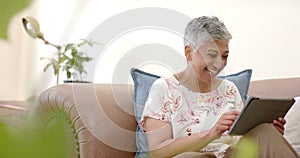 Happy senior biracial woman sitting on couch laughing and using tablet at home, slow motion
