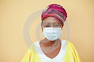 Happy senior black woman with face mask wearing traditional african dress - Focus on face