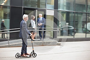 Happy senior businessman commuting to work on a kick scooter