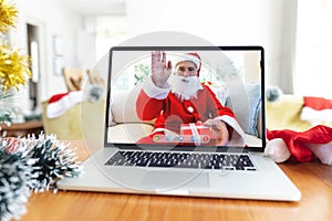 Happy senior caucasian man in santa costume waving on laptop video call screen at christmas time