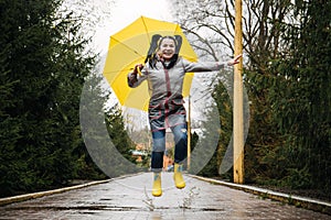 Happy senior cheerful mature, elderly, retired woman with yellow umbrella enjoying life at rainy day in park. Enjoy