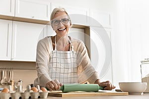 Happy senior chef woman wearing apron, making pastry in kitchen
