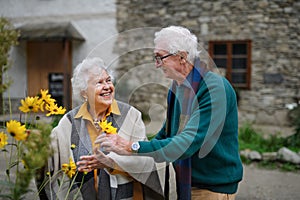 Happy senior couple at autumn city walk, posing with flowers.