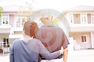 Happy senior couple from behind looking at front of house and car. Warm tone with sunlight.