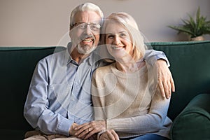 Happy senior couple bonding looking at camera sit on sofa