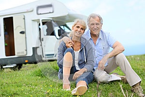 Happy senior couple with camping car sitting in grass