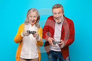 Happy senior couple in casual playing videogames over blue background