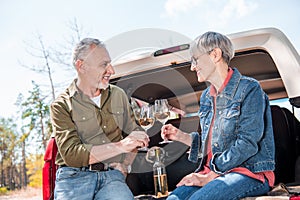 happy senior couple clinking wine glasses and looking at each other near car.