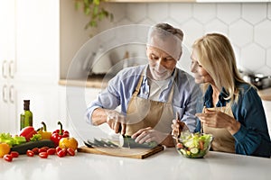 Happy senior couple cooking healthy meal together in kitchen interior