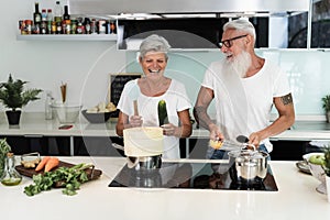 Happy senior couple dancing while cooking together at home - Focus on faces