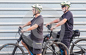 Happy senior couple doing together outdoor activity with electric bicycle. Healthy lifestyle. Yellow helmet, black clothes.