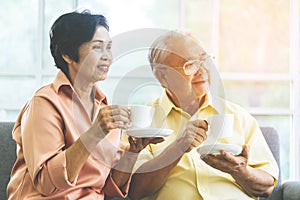 Happy senior couple drinking coffee on sofa at home looking out the windows peacefully