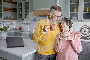 Happy senior couple drinking coffee or tea on home kitchen